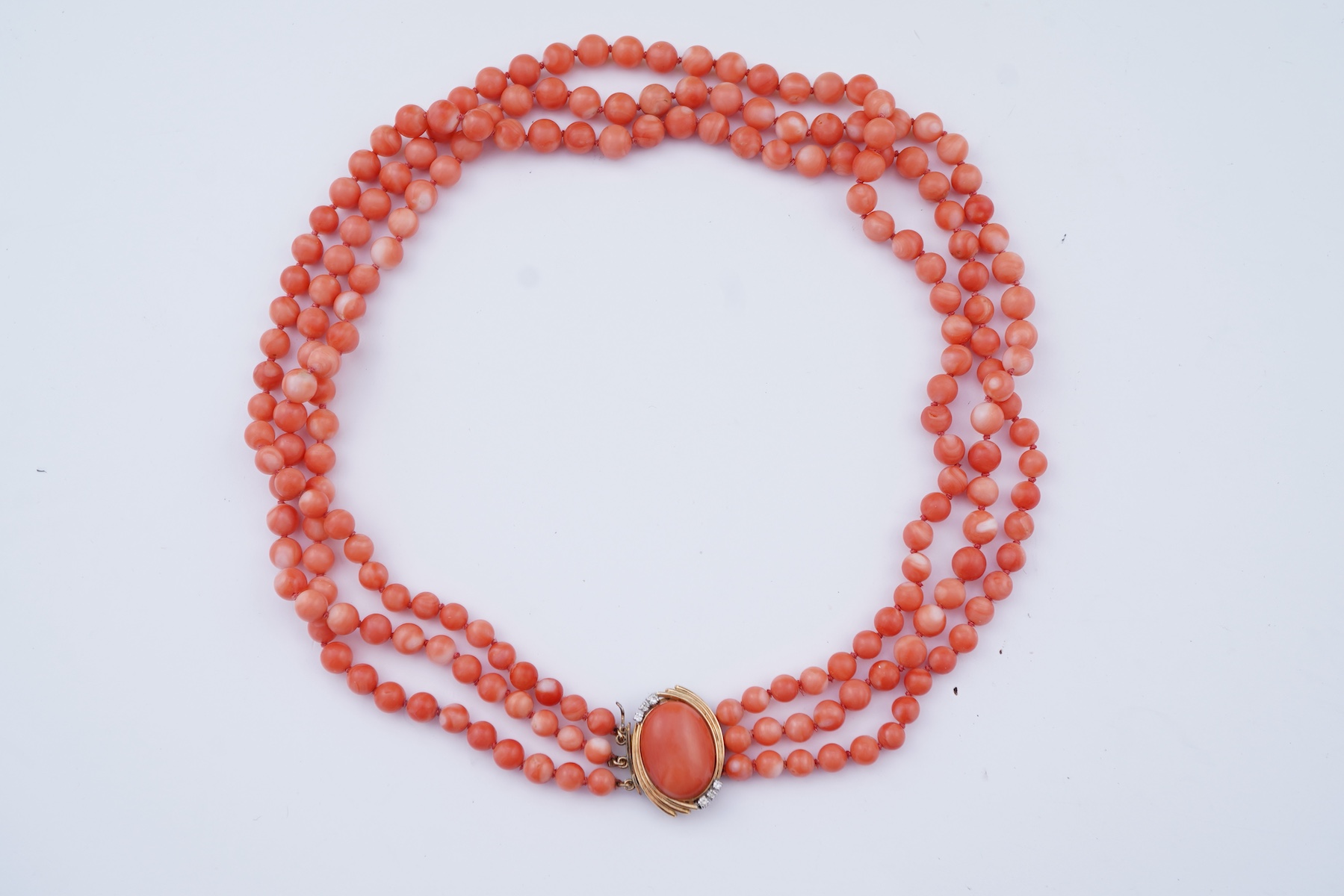 A coral necklace, composed of three strands of coral beads measuring approximately 5.1-6.6mm diameter, to a gold clasp set with a coral cabochon and brilliant-cut diamonds, mounted in gold, length 45.5cm, stamped 14K, ca